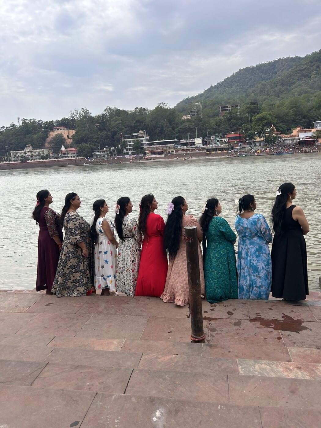Women standing beside the Ganga with the hills of Rishikesh beyond